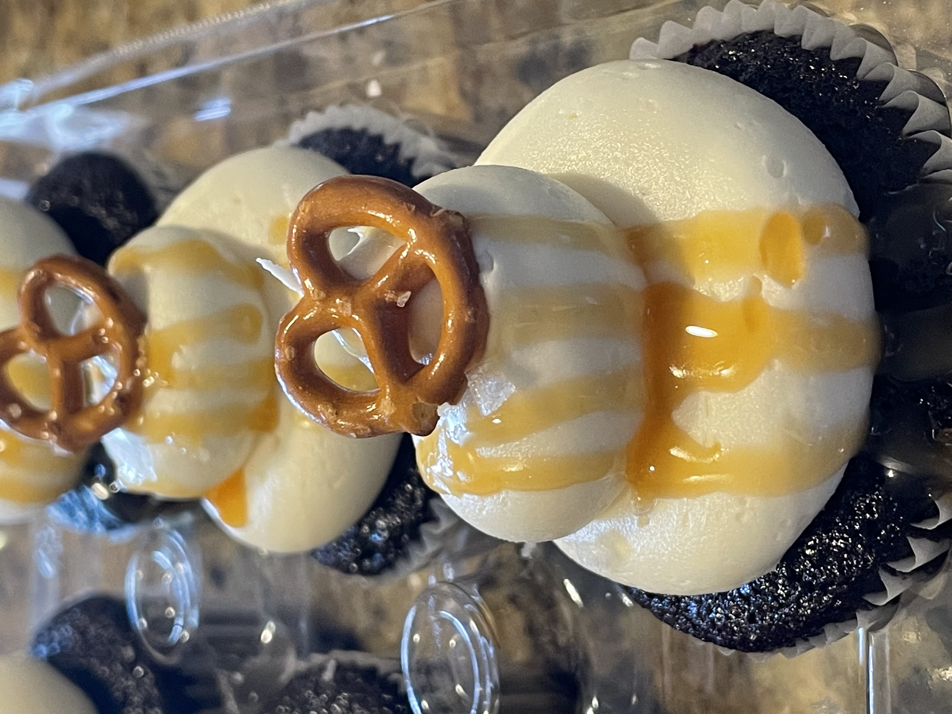 Dark chocolate cupcakes with white vanilla frosting, golden caramel drizzle, and a pretzel on top